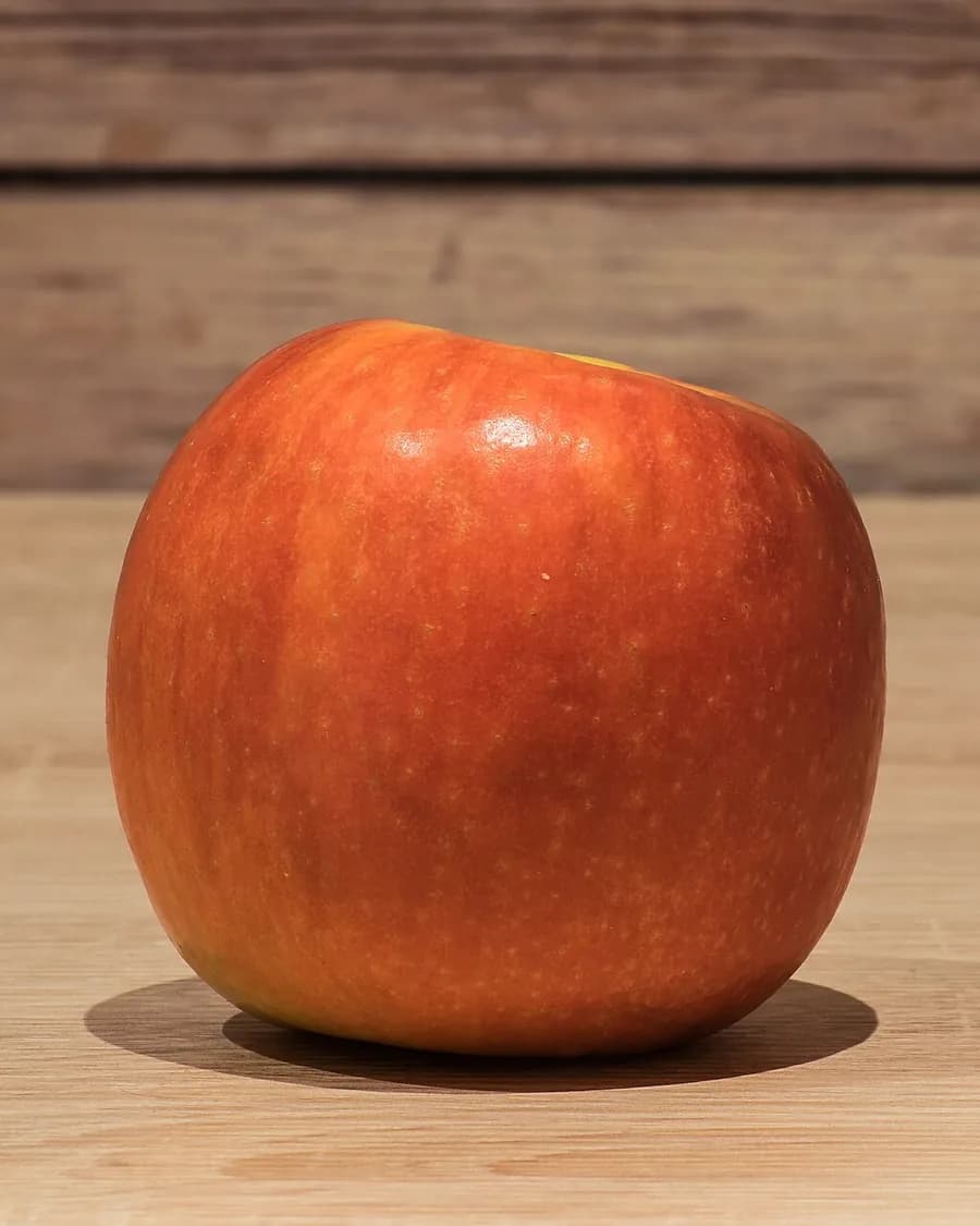 A polished red apple resting on a wooden counter